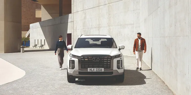 Imagen de dos peronas admirando el SUV Palisade estacionado un dia de sol.