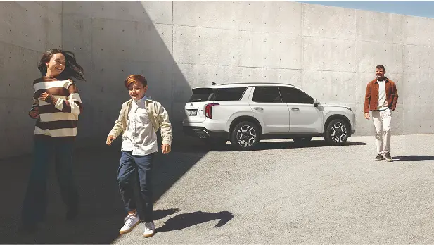 Imagen de un joven caminando desde su SUV Palisade un dia de sol.