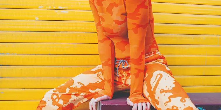 Imagen de una persona vestida de naranja sentada enfrente a una pared amarilla